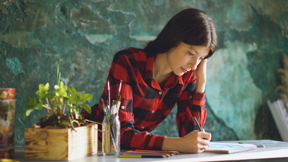 A woman drawing in a sketchbook at an art studio desk