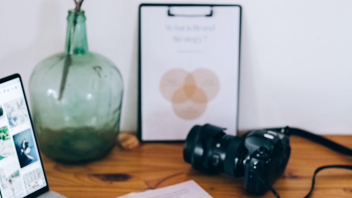 A camera, notebook and laptop on a creative work desk